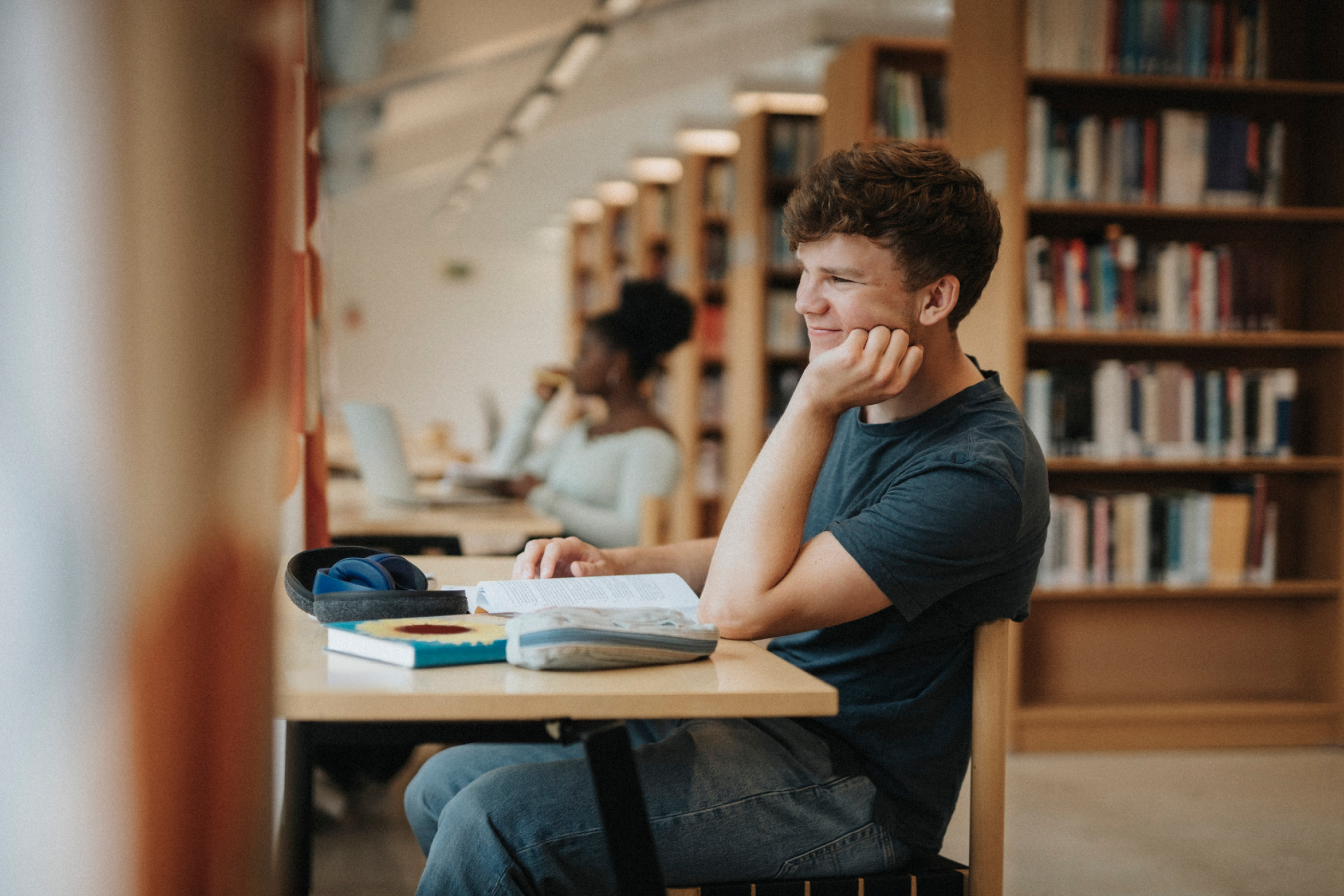 Um estudante a estudar numa secretária com livros e um portátil numa biblioteca.