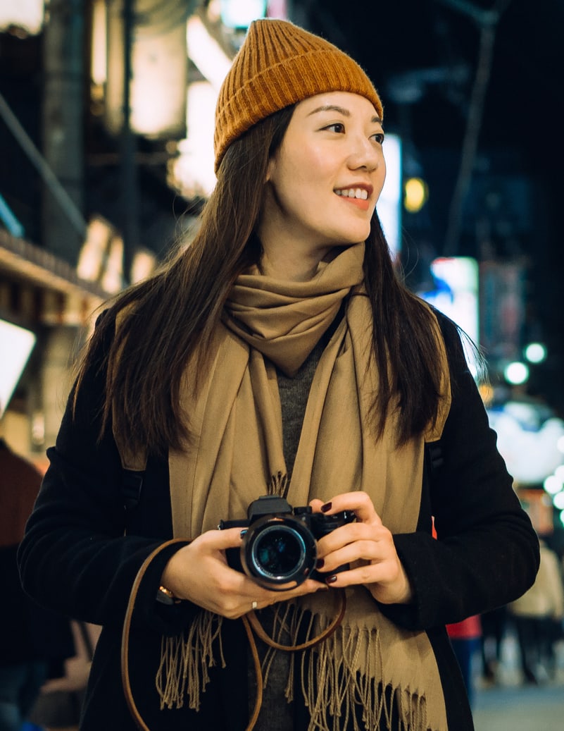 Uma jovem mulher de chapéu segura uma câmara à noite